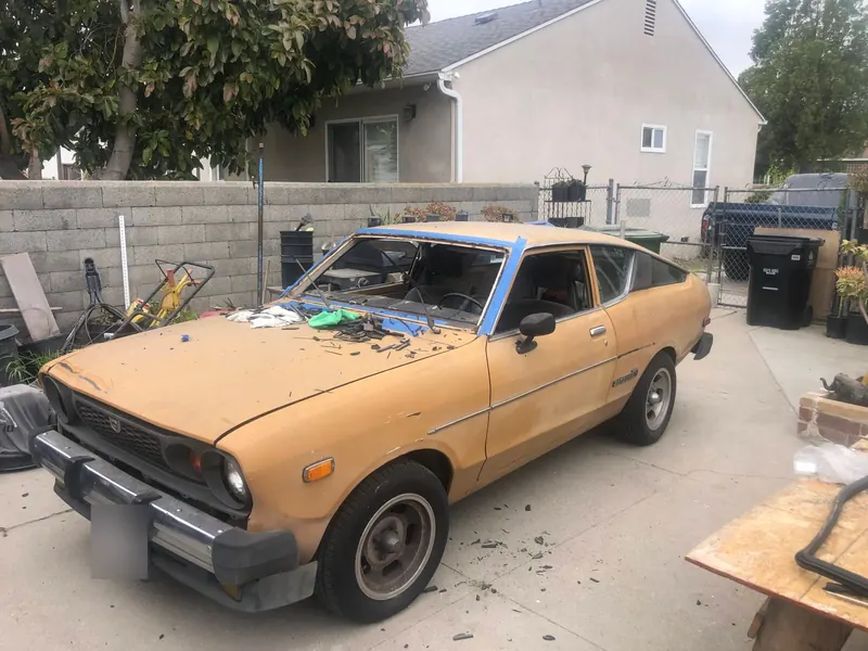 Classic Datsun hatchback with its old windshield removed for replacement