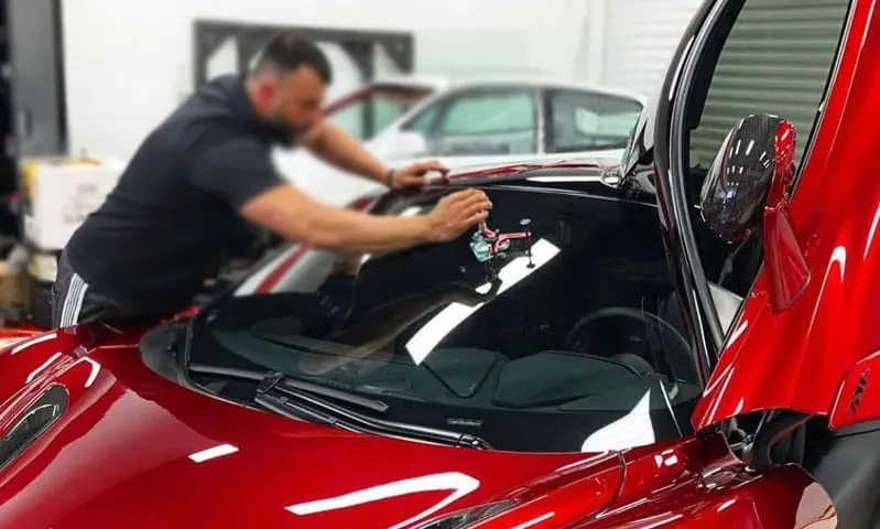Technician repairing a windshield chip on a red McLaren supercar