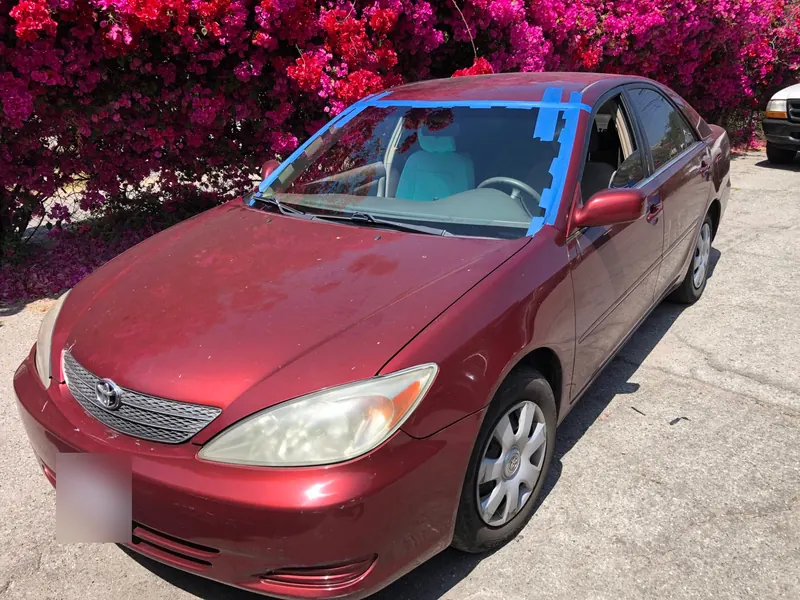 Red Toyota Camry with a newly installed windshield taped in place, parked in Los Angeles